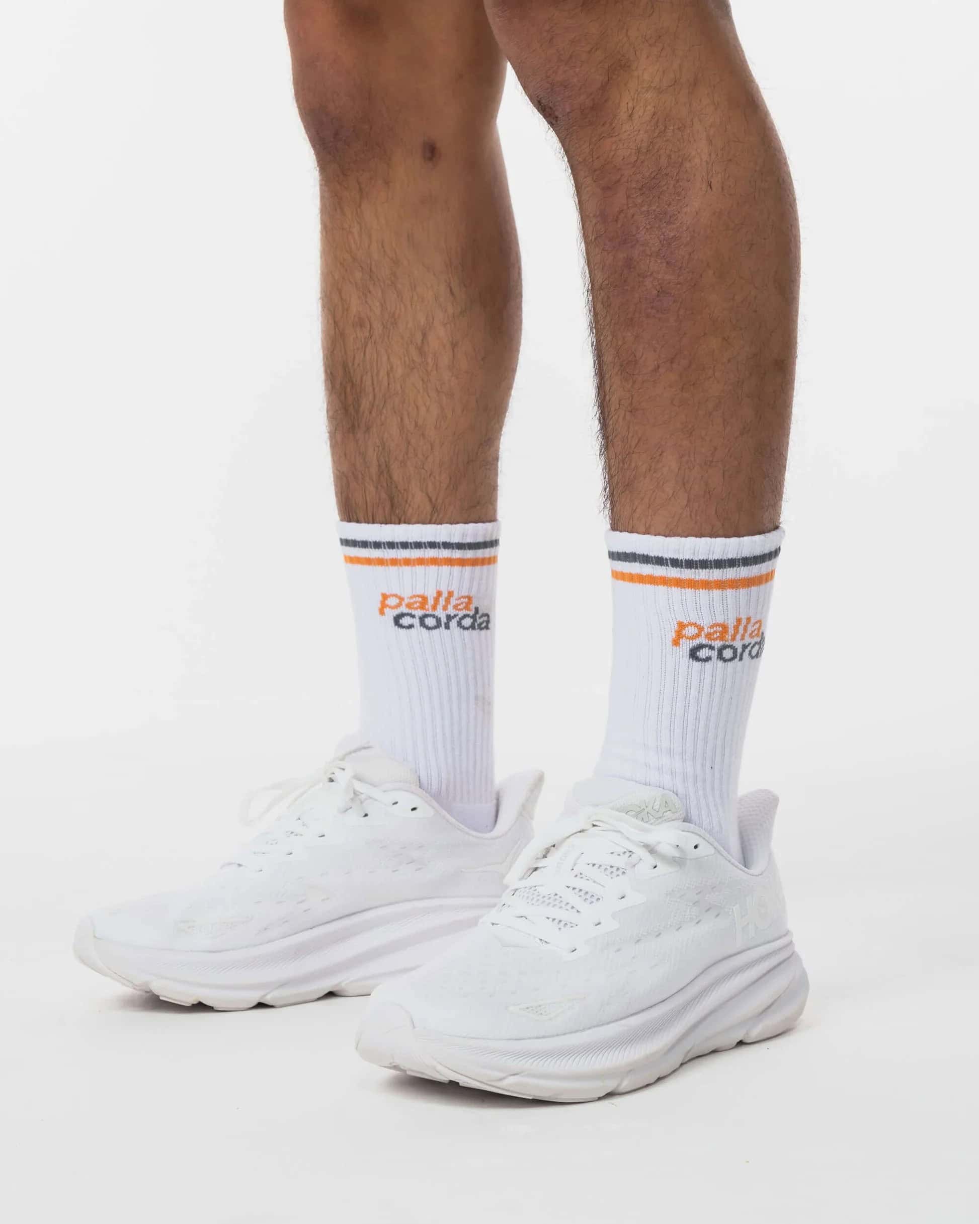 Close-up of men's white sneakers and socks on a plain background.